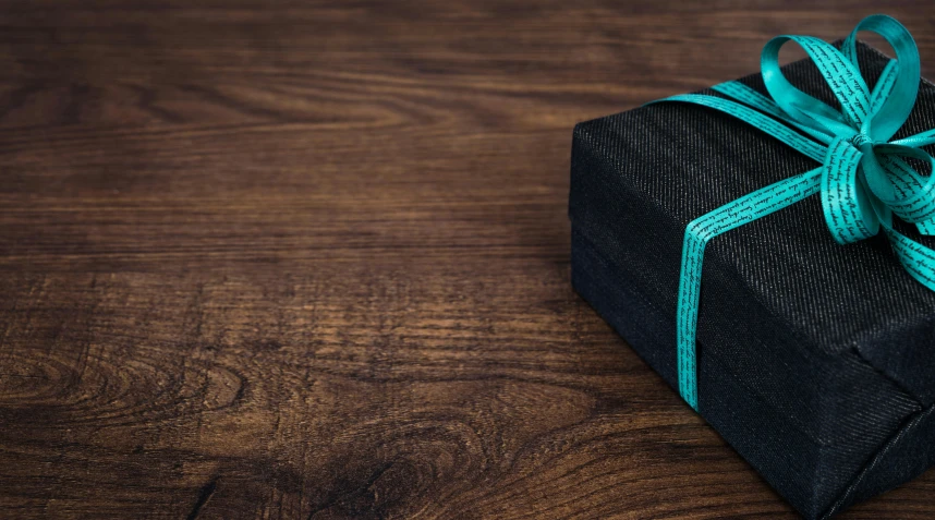 a wrapped gift sitting on top of a wooden table, pexels contest winner, black and teal paper, carbon fibers, webbing, high-resolution