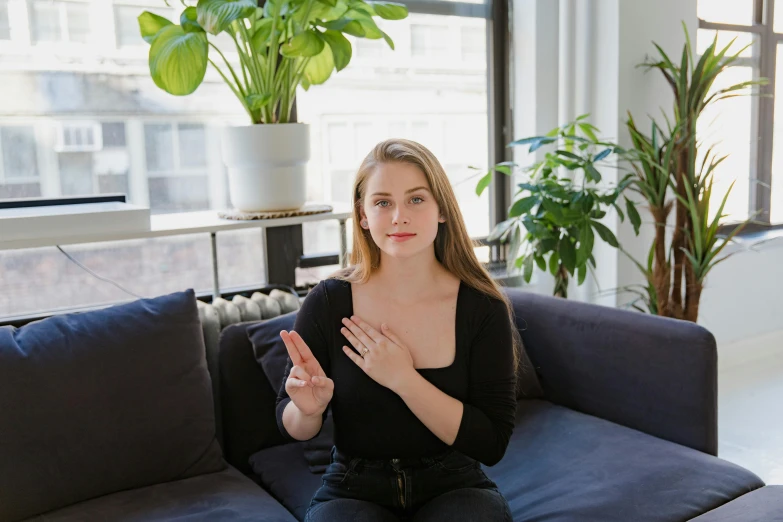 a woman sitting on a couch in a living room, a portrait, unsplash, hand gestures, sydney sweeney, low quality photo, bright daylight indoor photo