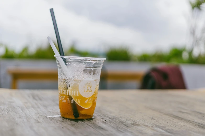 a plastic cup sitting on top of a wooden table, unsplash, iced tea glass, al fresco, low quality photo, te pae