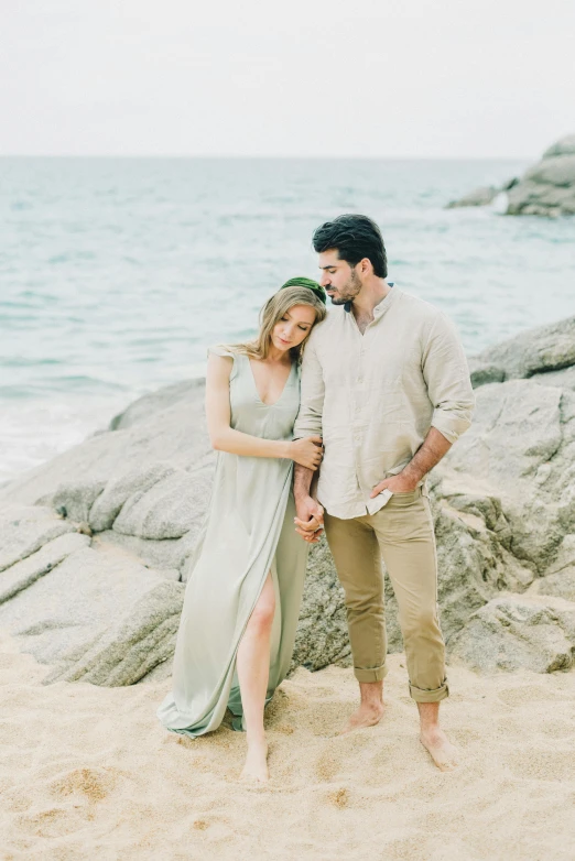 a man and woman standing next to each other on a beach, a picture, by Nicolette Macnamara, unsplash, renaissance, boho neutral colors, standing on rocky ground, sea - green and white clothes, soft elegant gown