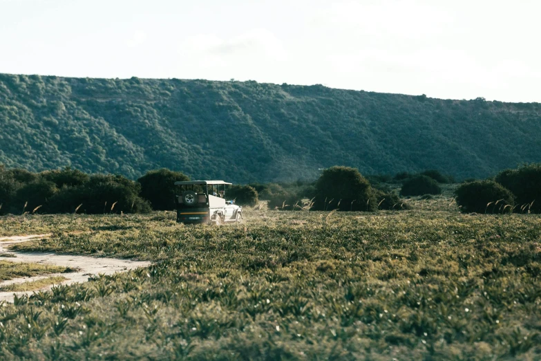 a truck driving down a dirt road next to a lush green hillside, a polaroid photo, unsplash, land art, abandoned bus stop, bulli, on the coast, 2000s photo