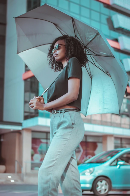 a woman walking down the street holding an umbrella, by Ingrida Kadaka, trending on unsplash, wearing pants and a t-shirt, fashion model features, essence, with teal clothes