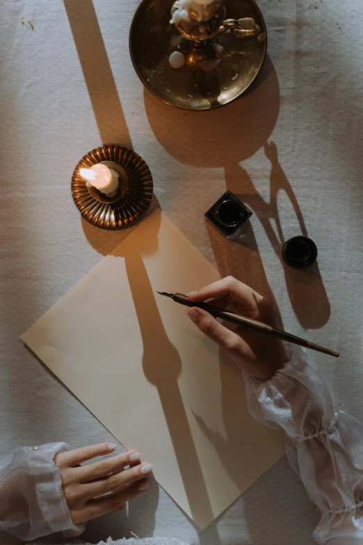 a person writing on a piece of paper next to a candle, visual art, shadow and light, flatlay, brown, gold