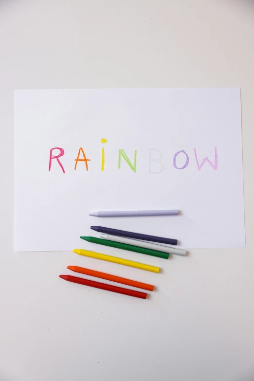 a rainbow of colored pencils sitting on top of a piece of paper, a child's drawing, in white lettering, drawn on white parchment paper, raindrop, official product photo