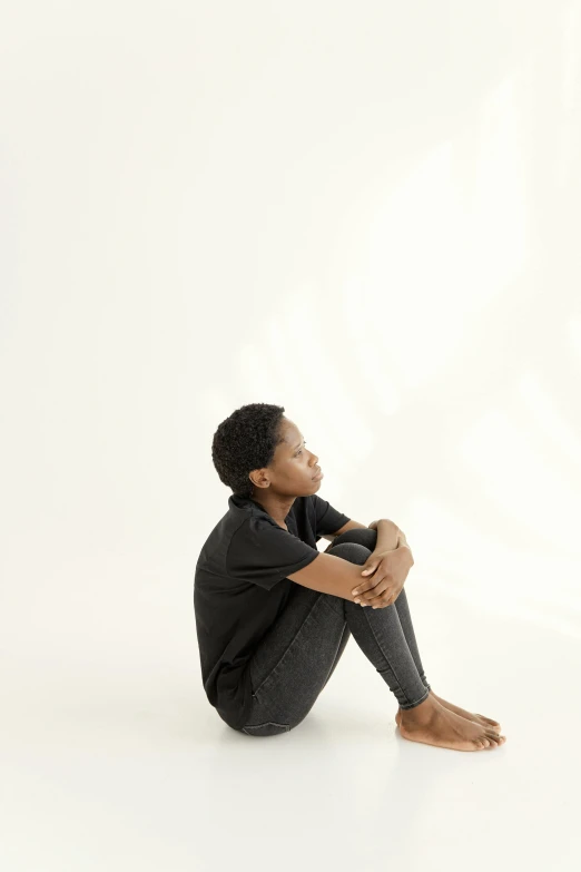 a woman sitting on the ground with her legs crossed, black teenage boy, sitting in an empty white room, promo image, reflecting light