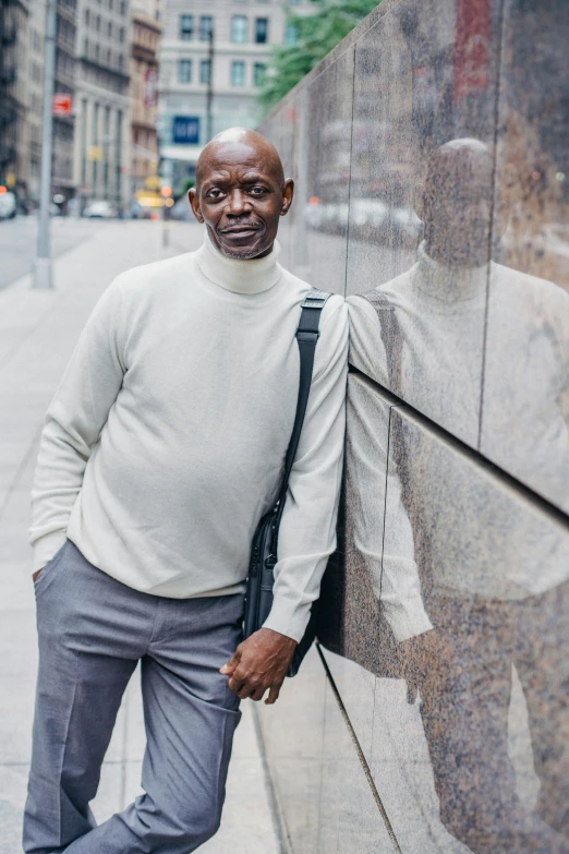 a man leaning against a wall on a city street, by William Berra, pexels contest winner, portrait of samuel l. jackson, tall and lanky skinny, an elderly, wearing turtleneck