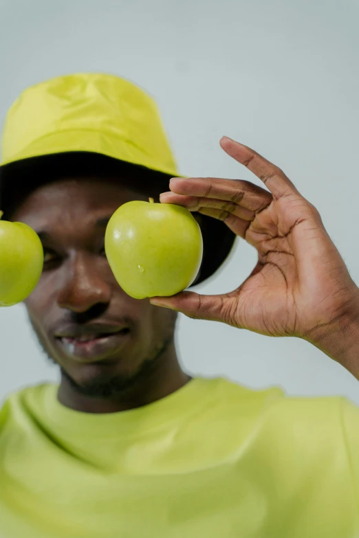 a man holding three apples in front of his face, unsplash, visual art, wearing hi vis clothing, adut akech, wearing a silly hat, yellow pupils