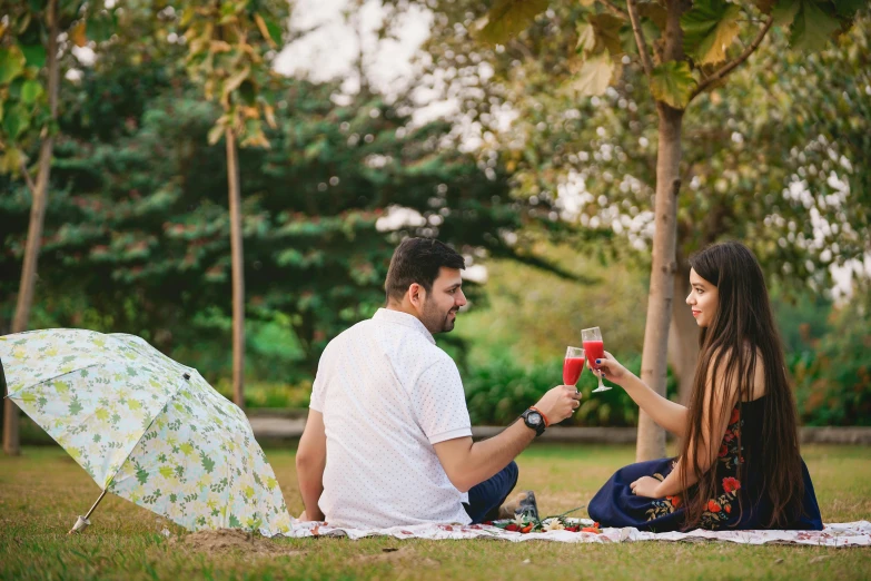 a man and a woman sitting on a blanket with umbrellas, pexels, botanic garden, drink, ad image, half image