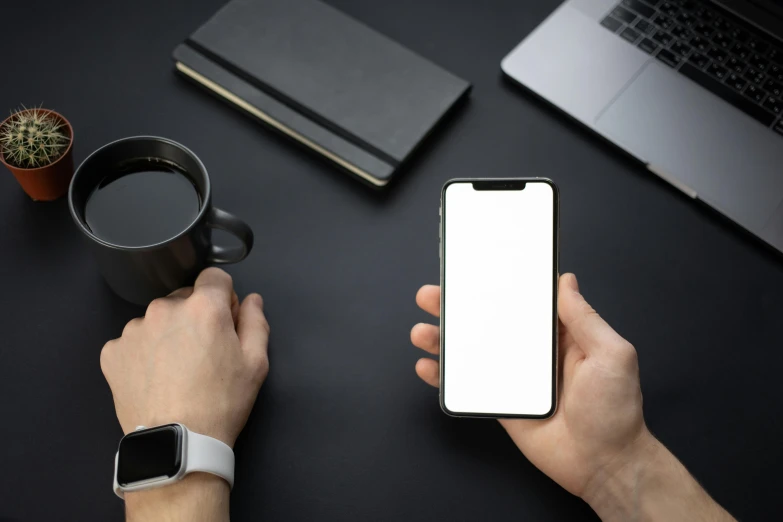 a person holding a smart phone next to a laptop and a cup of coffee, trending on pexels, square, standing with a black background, on a white table, no - text no - logo