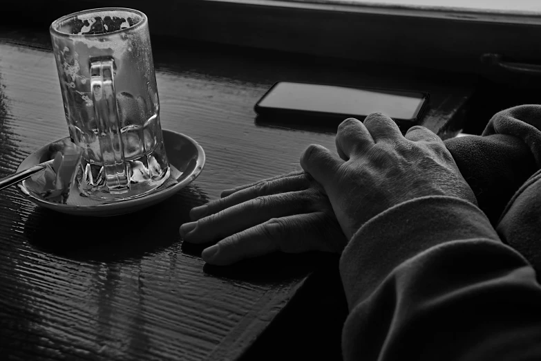 a person sitting at a table with a glass of water, a black and white photo, comforting, phone in hand, holding hands, chilly dark mood