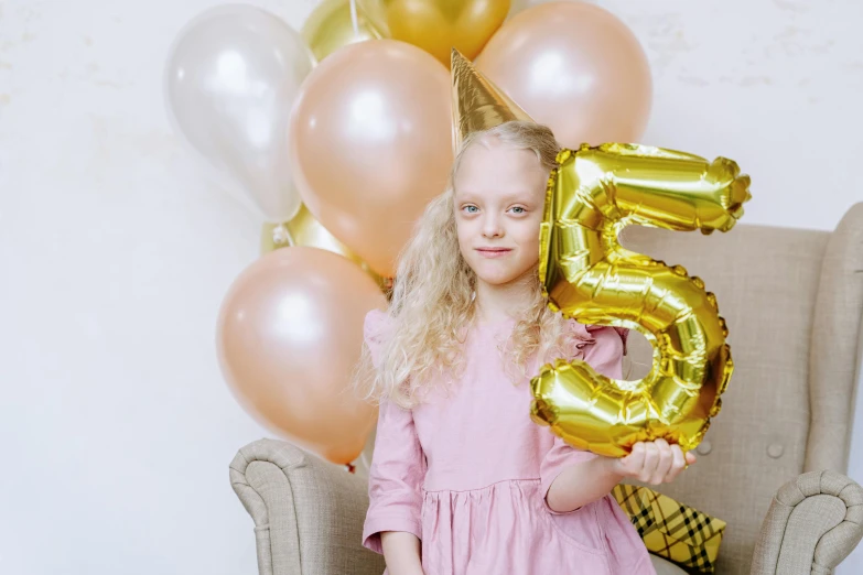 a little girl sitting in a chair holding a number five balloon, pexels contest winner, golden colour, greta thunberg, party balloons, thumbnail