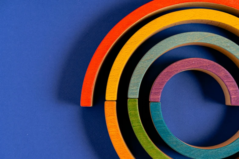 a group of colorful wooden rings on a blue surface, an abstract sculpture, by Doug Ohlson, pexels contest winner, op art, enso, architectural scale, rainbow coloured rockets, vibrant: 0.75