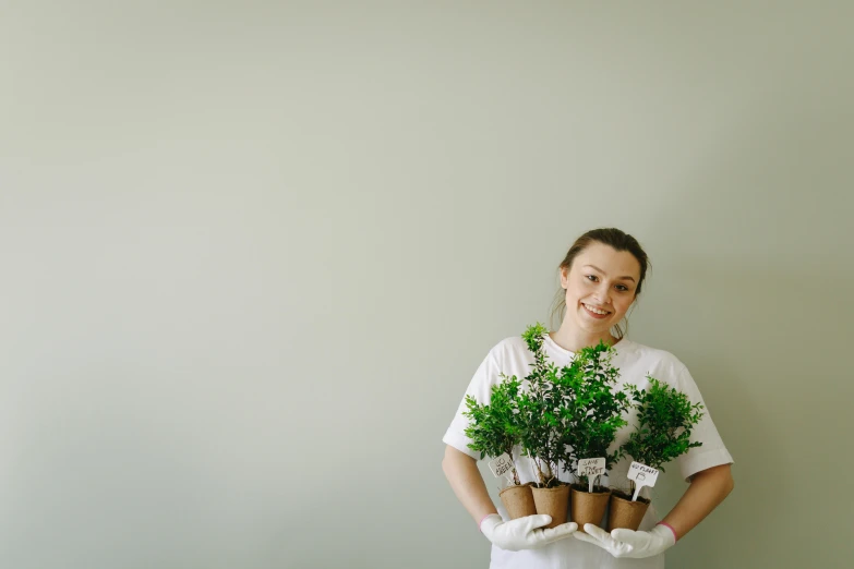 a woman holding a bunch of potted plants, dressed in a white t shirt, background image, cardboard, portrait image