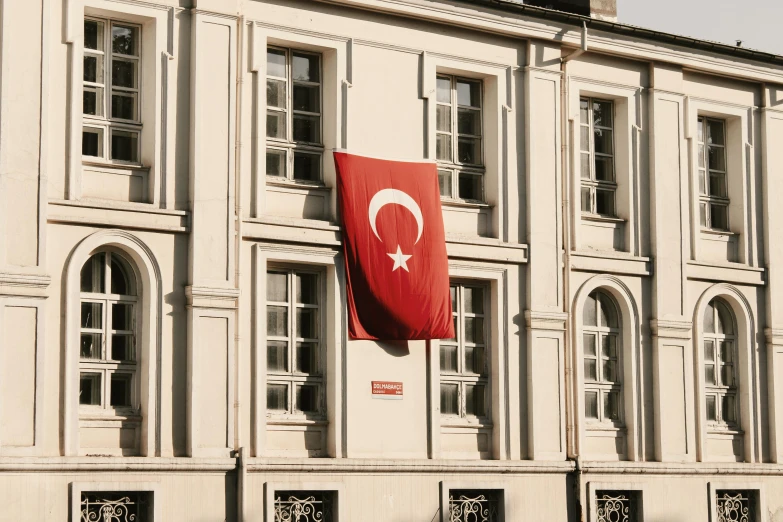 a large flag hanging from the side of a building, inspired by Géza Mészöly, pexels, hurufiyya, turkey, square, private school, white