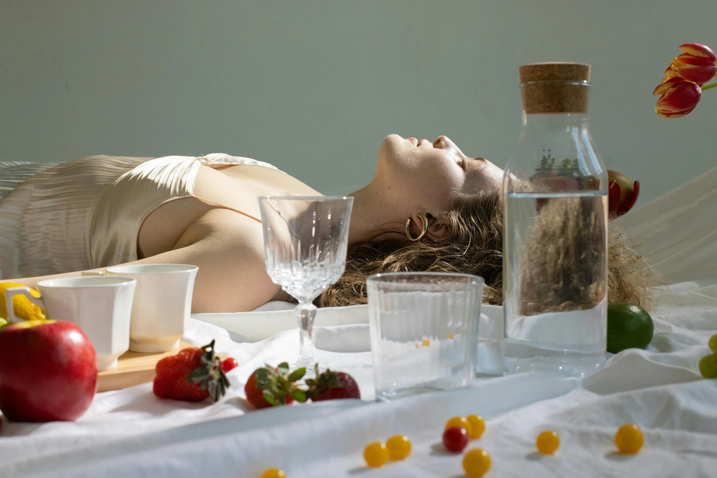 a woman laying on a bed next to a bottle of water, inspired by Konstantin Somov, unsplash, hyperrealism, molecular gastronomy, white tablecloth, ignant, strange ingredients on the table