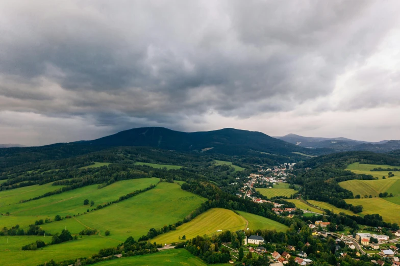 an aerial view of a small town in the mountains, pexels contest winner, storm clouds in the distance, green fields, slide show, ultrawide landscape