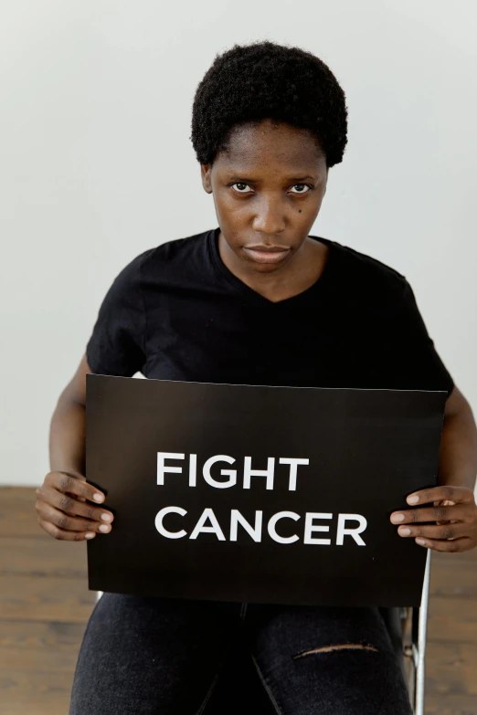 a woman sitting in a chair holding a sign that says fight cancer, an album cover, pexels contest winner, renaissance, dark-skinned, fighting stance, closeup photograph, scientific photo