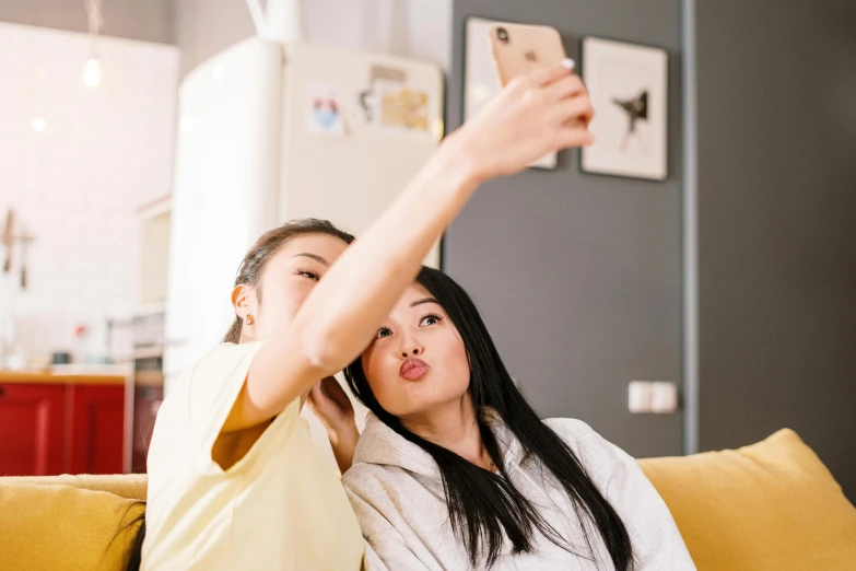 a man and a woman sitting on a couch taking a selfie, trending on pexels, asian women, woman holding another woman, tongue sticking out, avatar image