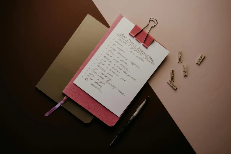 a notepad sitting on top of a piece of paper, by Carey Morris, trending on unsplash, maroon metallic accents, pink scheme, writing on a clipboard, thumbnail