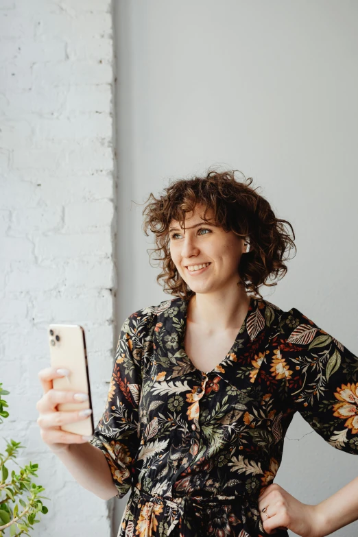 a woman standing in front of a window holding a cell phone, a picture, trending on pexels, renaissance, curly bangs, studio portrait, next to a plant, curly brown hair