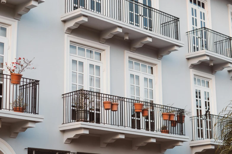 a building with a bunch of balconies on the balconies, by Carey Morris, pexels contest winner, neoclassicism, steel window mullions, white houses, flat grey color, pots with plants