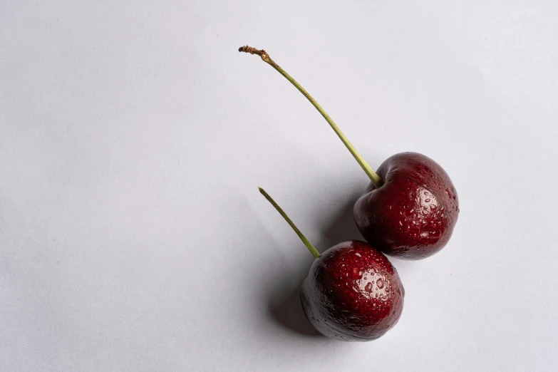 two cherries sitting on top of a white surface, by Peter Churcher, unsplash, background image, high quality product image”