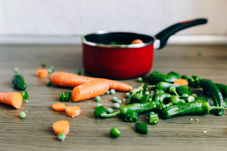 a wooden table topped with carrots and peas, by Daniel Lieske, pexels contest winner, pots and pans, background image, enamel, red and green color scheme