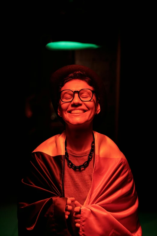 a woman wrapped in a blanket in a dark room, an album cover, pexels contest winner, wearing gold glasses, mutahar laughing, red and green lighting, androgynous person