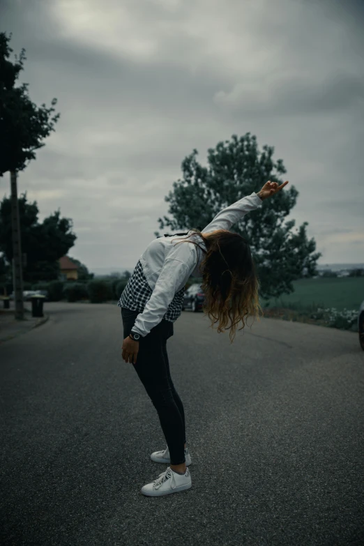 a woman doing a handstand in the middle of the road, pexels contest winner, happening, grey sky, wearing a track suit, looking left, waving