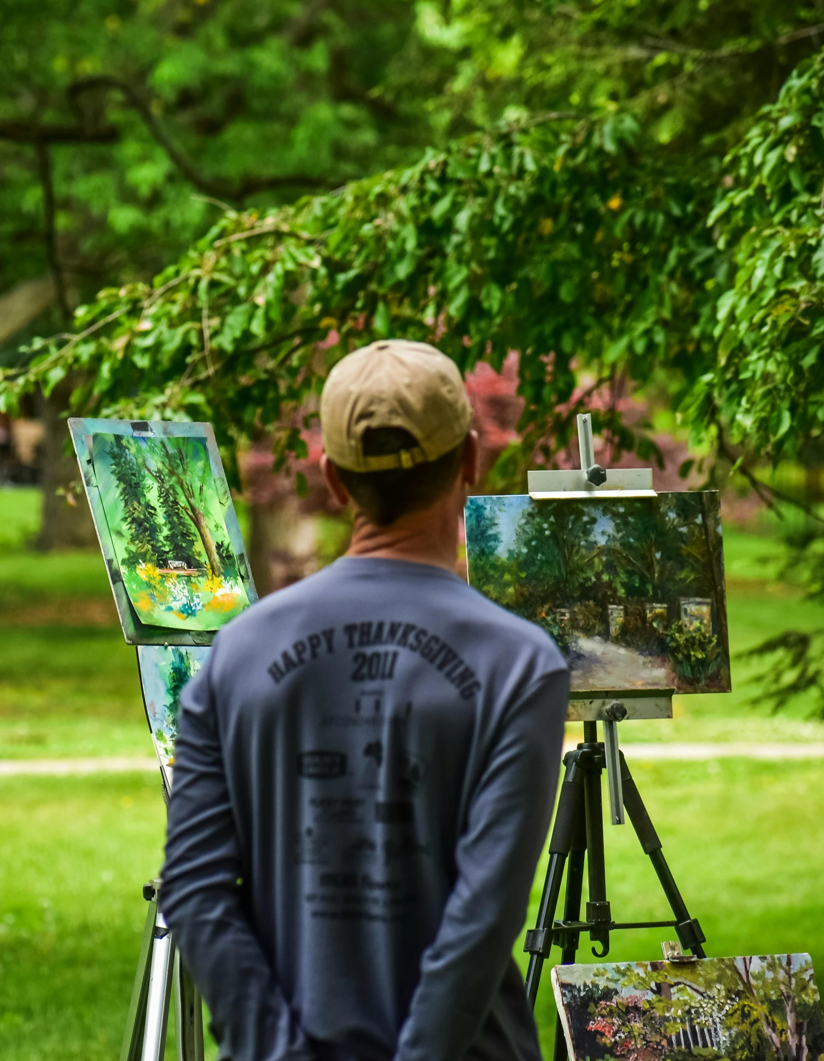 a man standing in front of a painting on a easel, inspired by Willard Metcalf, unsplash contest winner, plein air, trees in foreground, shot from the back, park in background, museum quality photo