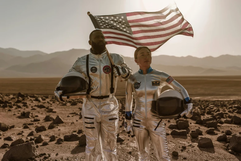 two people in space suits holding an american flag, pexels contest winner, afrofuturism, stargate standing in desert, venus project, asteroids realistic cinematic, diverse costumes