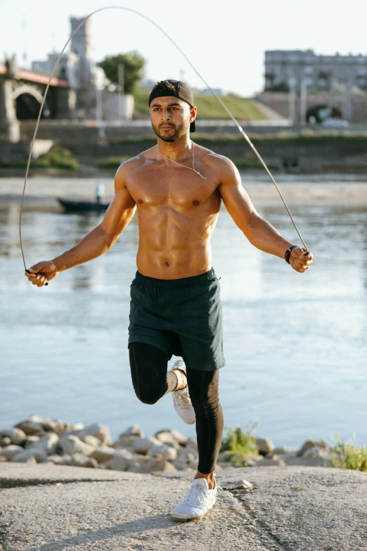 a man doing a jump rope exercise in front of a body of water, trending on pexels, renaissance, mid-shot of a hunky, islamic, wearing tank top, good looking face