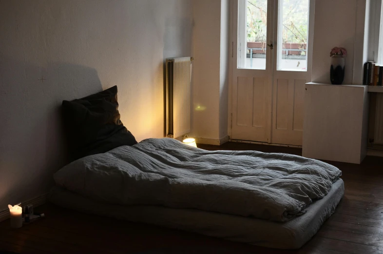 a bed sitting on top of a wooden floor next to a window, by Daniel Lieske, light and space, kreuzberg, soft outdoor light, grey, single light