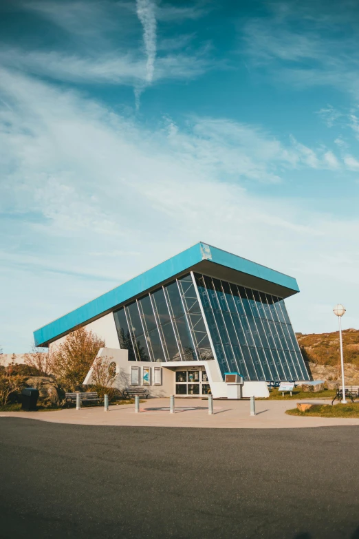 a blue and white building sitting on the side of a road, by Lee Loughridge, unsplash, brutalism, teal energy, sportspalast amphitheatre, slate, built around ocean
