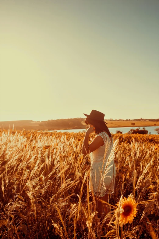 a woman standing in a field of tall grass, pexels contest winner, an australian summer landscape, golden colors, gazing at the water, farming