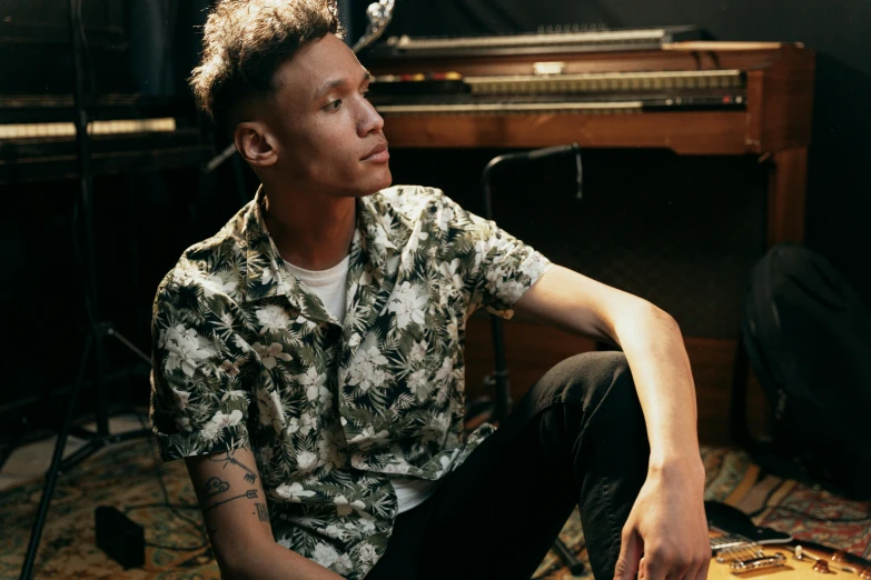 a young man sitting in front of a piano, an album cover, unsplash, with hawaiian shirt, androgynous person, looking to the side off camera, brittney lee