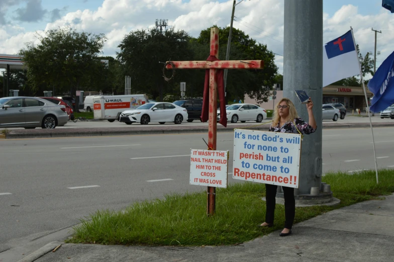 a woman holding a sign on the side of the road, a photo, by John Luke, renaissance, crucifix, florida man, holding a red banner, placards