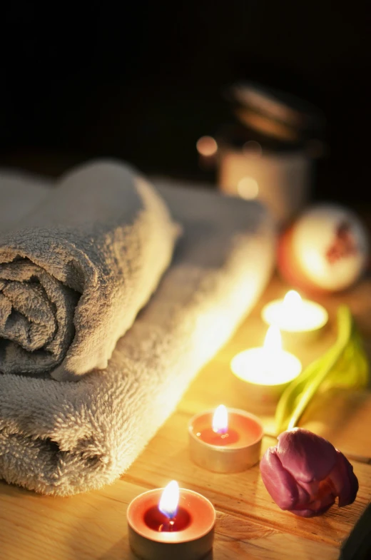 a couple of towels sitting on top of a wooden table, dark lit candles, square, flowers, close up photograph