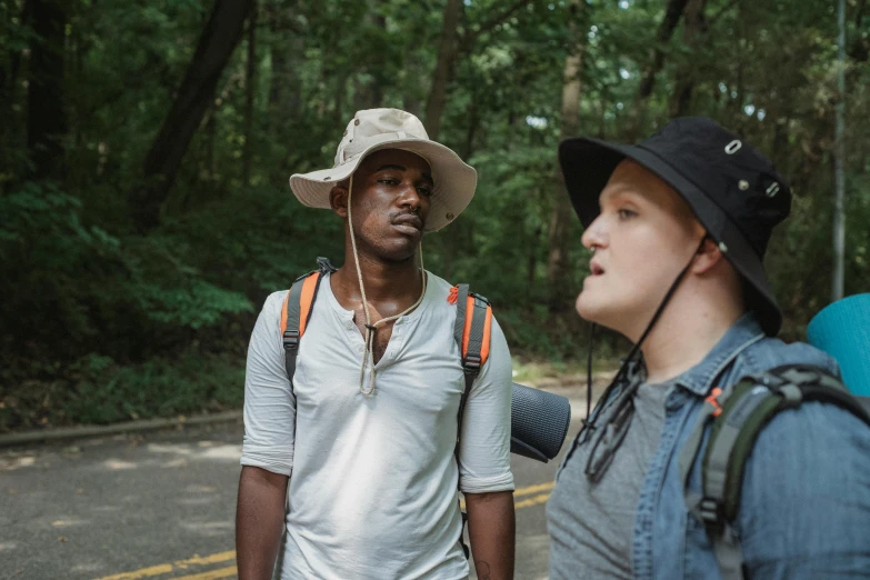 a couple of men standing next to each other on a road, by Carey Morris, trekking in a forest, with rap cap on head, black man, kyle hotz