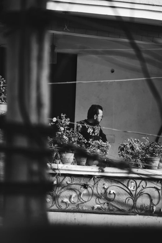 a black and white photo of a woman on a balcony, unsplash, happening, small plants on the window sill, with his long black hair, surveillance, at the counter