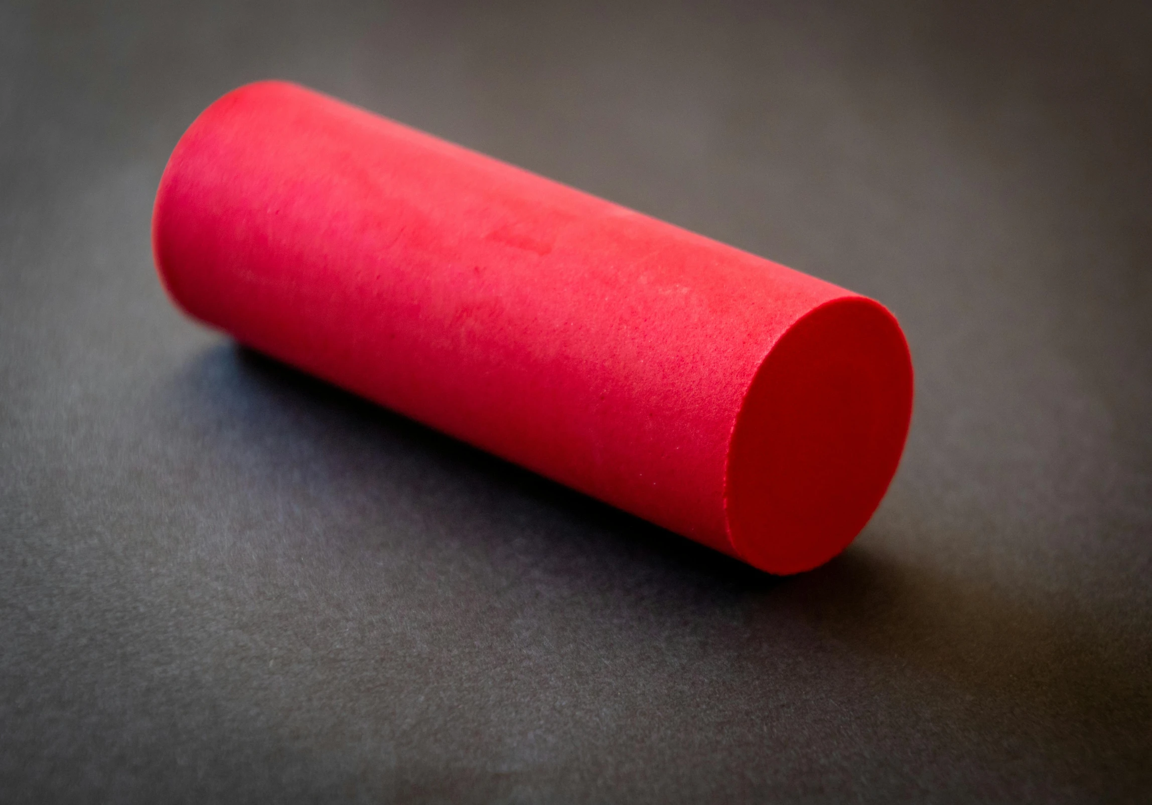 a red tube sitting on top of a table, on black paper, play-doh, soft surface texture, round corners