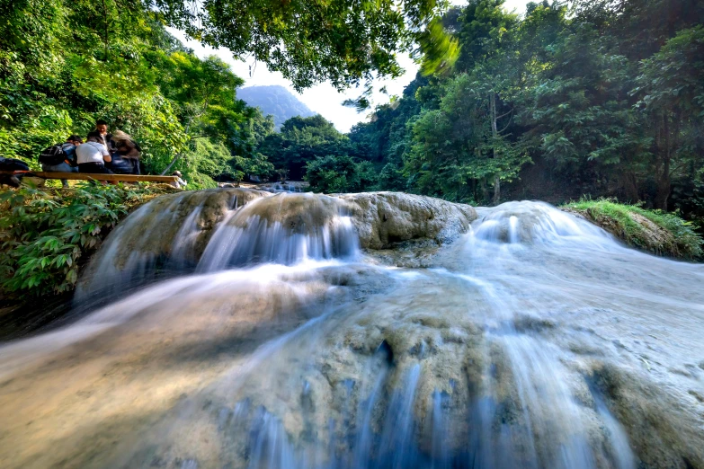 a couple sitting on a bench next to a waterfall, pexels contest winner, sumatraism, avatar image, river running through it, jamaica, panoramic shot