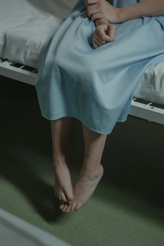 a woman in a blue dress sitting on a bed, by Elsa Bleda, trending on reddit, focus on his foot, wearing a hospital gown, long thin legs, paul barson