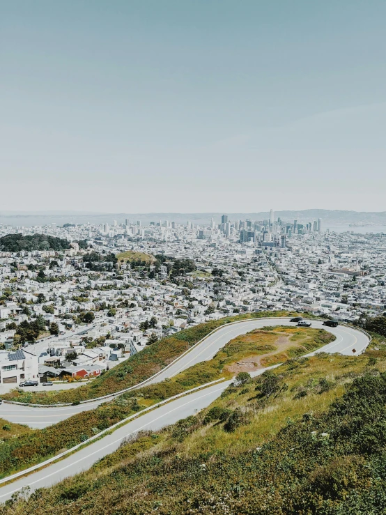 a view of a city from the top of a hill, by Carey Morris, unsplash contest winner, overlooking sf from twin peaks, ignant, road trip, grass field surrounding the city