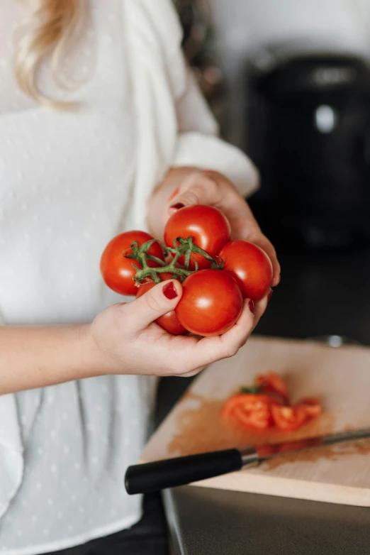 a woman holding a bunch of tomatoes in her hands, a still life, by Julia Pishtar, pexels contest winner, in the kitchen, round-cropped, multiple stories, made of glazed