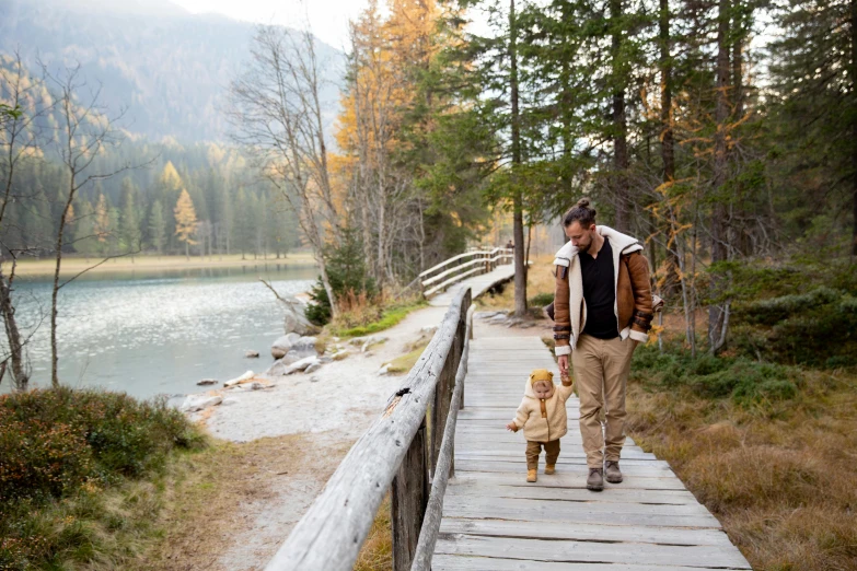 a man walking a dog across a wooden bridge, by Sebastian Spreng, pexels contest winner, father holds child in the hand, lago di sorapis, leather clothing and boots, autum