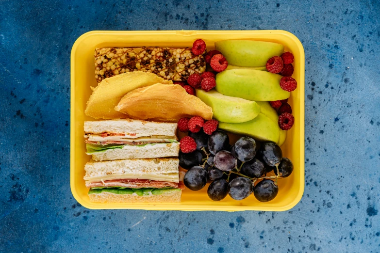 a plastic container filled with a sandwich and fruit, by Carey Morris, pexels, square, yellow, schools, grape