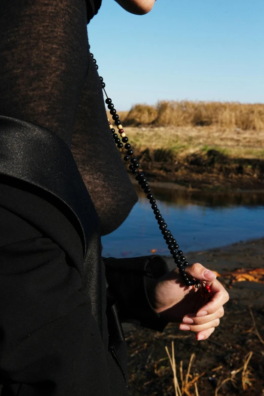 a woman standing next to a body of water, an album cover, inspired by Modest Urgell, unsplash, renaissance, beads cross onbare chest, black turtleneck, farming, photographed for reuters