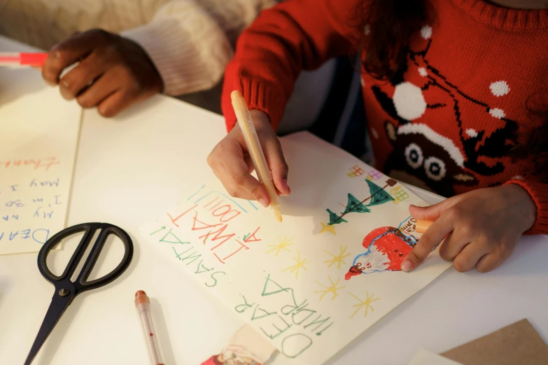 a child holding a pencil and writing on a piece of paper, a child's drawing, by Julia Pishtar, wearing festive clothing, santa, high angle close up shot, promotional image