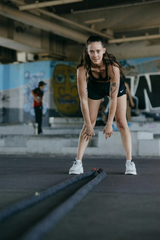 a woman squatting on a rope in a gym, a portrait, pexels contest winner, happening, rollerbladers, gif, standing on rooftop, wearing black shorts